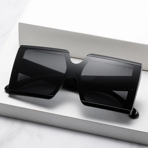 Modern oversized square sunglasses with black glossy frames on white geometric stones
