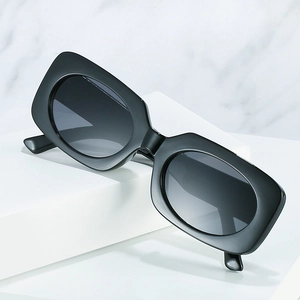 Retro black wide frame sunglasses with dark gradient lenses on a white stone pedestal