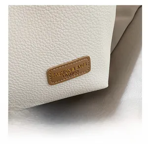 Detail of white lychee grain leather tote with a stitched brown fashion label tag