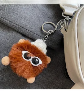 Detail view of a cute brown plush pompom charm hanging on a stylish white leather handbag