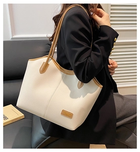 Detail of cream pebbled leather tote with brown straps and brand label on a black blazer