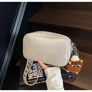 Detail of white rectangle crossbody bag with geometric wide strap and plush charm decor