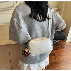 Detail shot of off-white crossbody bag with wide strap and cute brown teddy bear charm