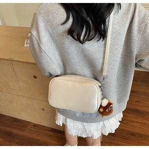 Detail of off-white leather crossbody bag with wide strap and brown plush charm