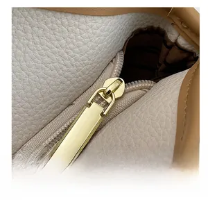 Close-up of golden metal zipper and lychee grain leather texture on a beige tote bag