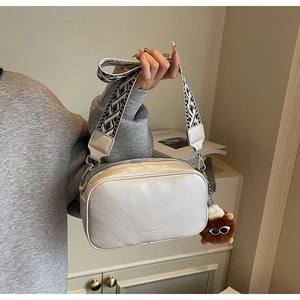 Chic white crossbody bag featuring a geometric wide strap and cute plush charm detail