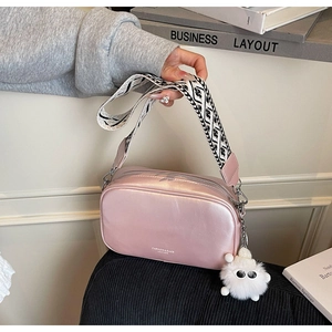 Detail of bright pink square bag with black and white geometric wide strap and plush ball