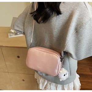 Detail of light pink metallic crossbody bag with a white plush charm on model