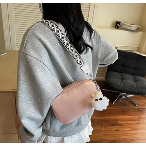 Detail of pink crossbody bag with geometric strap and white plush doll pendant accessory