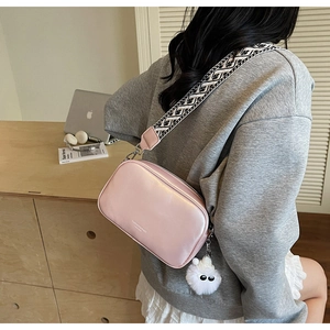 Pink crossbody square bag featuring a geometric wide strap and cute plush charm detail