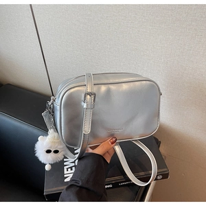 Close-up of silver textured crossbody bag with metal finish and white pompom charm
