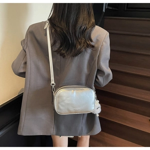Model wearing a silver metallic crossbody square bag with a cute plush monster charm