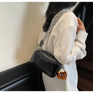 Detail of black glossy crossbody bag with geometric wide strap and plush charm