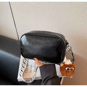 Detail of black crossbody bag with geometric wide strap and brown plush monster charm