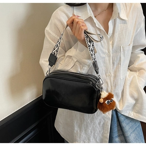 Detail of glossy black crossbody bag with geometric wide strap and plush monster charm