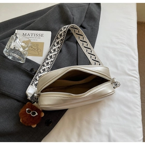 Chic cream camera bag detail with embroidered wide strap and cute plush charm