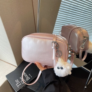 Pink minimalist crossbody square bag with plush charm on a book against a mirror