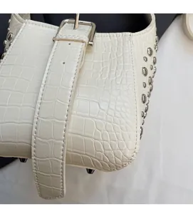 Close-up of white crocodile embossed leather bag with silver rivet studs and metal buckle