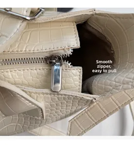 Macro shot of smooth silver metal zipper on cream crocodile-embossed leather handbag
