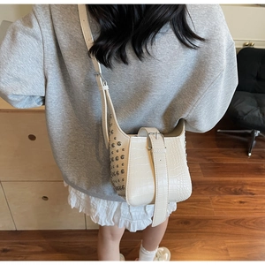 Detail of off-white crocodile embossed bucket bag with silver rivet studs on the side