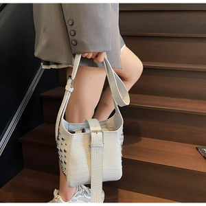 Detail of white crocodile pattern bucket bag with silver stud rivets and wide shoulder strap