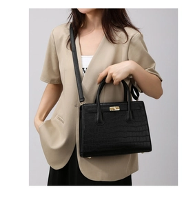 Detail of black crocodile pattern handbag with gold twist lock and elegant top handles