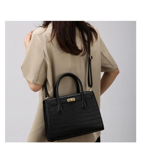 Detail of black crocodile texture handbag with gold rotary lock and top handles