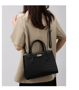 Detail of black crocodile texture handbag with gold twist-lock and adjustable strap