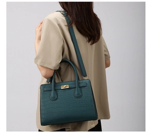 Detail of dark green crocodile pattern handbag with metal turn-lock and adjustable strap