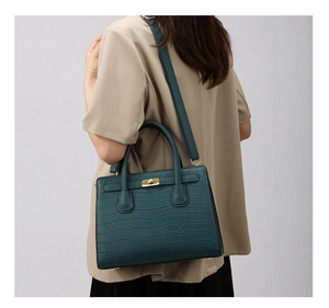 Detail of dark green crocodile pattern handbag with gold twist lock and shoulder strap