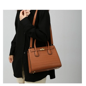 Detail of a brown crocodile pattern handbag with golden twist lock and twin handles