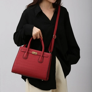 Detail of red croc-embossed handbag with gold metal clasp worn by a fashion model