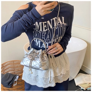 Silver quilted bucket bag with chain strap and metal handle held by model in interior