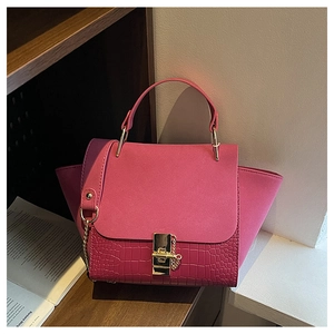 Close-up of pink faux-crocodile bag with gold metal lock and chain on wooden shelf