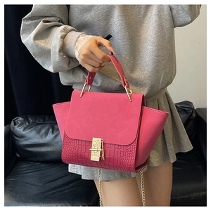 Detail of rose red crocodile texture bag with gold handle and suede flap on black leather