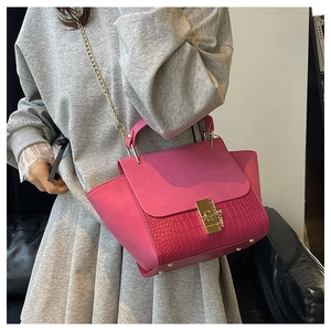Detail of fuchsia wing bag featuring crocodile texture, gold lock, and chain strap