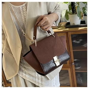 Detail of crocodile embossed leather handbag with gold chain strap and metal clasp lock