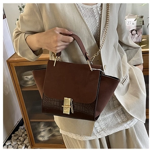 Detail of dark brown crocodile pattern handbag with vintage gold buckle and metal chain