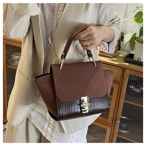 Detail of a brown croc-effect flap bag with golden metal chain and twist lock closure