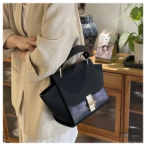Close-up of black crocodile pattern leather bag with gold chain strap on shoulder