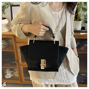 Detail of black crocodile texture bag with gold chain and matte panel in home setting