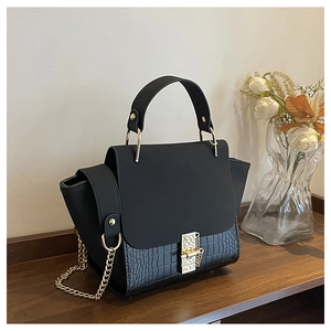 Detail of black handbag with crocodile texture, gold chain strap and metallic buckle