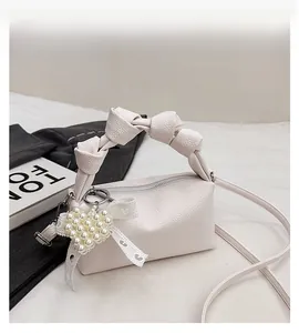 Close-up of cream leather bag with knotted handle, pearl heart charm and lace bow details