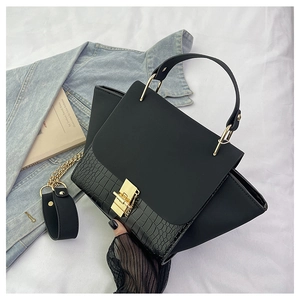 Close-up of black crocodile pattern leather bag with gold metal lock on white fabric
