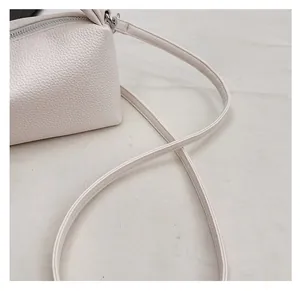 Detail of cream crossbody bag showing litchi texture surface and silver metal zipper