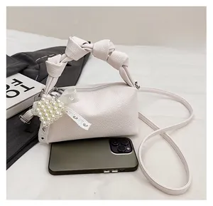 Mini cream hobo bag with braided handle and pearl charm detail next to a smartphone