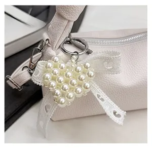 Detail of heart pearl bag charm with white lace bow and silver metal clasp hanging on bag