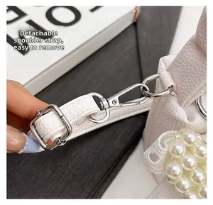 Detail of white textured leather bag with detachable strap and silver metal hooks