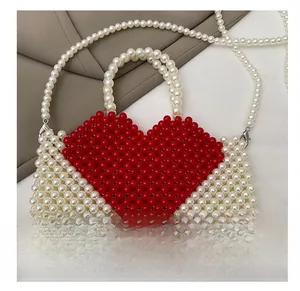 Detail of white beaded handbag featuring a red heart pattern and beaded shoulder strap