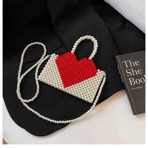 Detail of handmade beaded heart handbag with red pearls on a white woven base